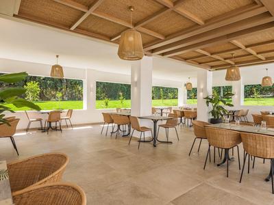 Offener Speiseraum mit Holzmöbeln, großen Fenstern und Pflanzen, hell und luftig gestaltet.