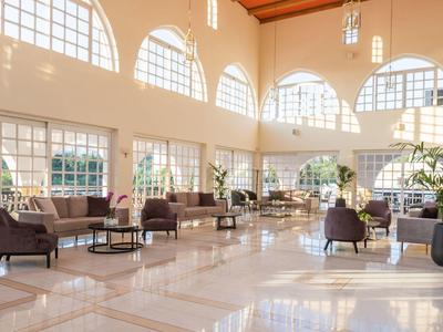 Heller, großzügiger Lobbybereich mit hohen Fenstern, Lederstühlen und glänzendem Marmorboden.