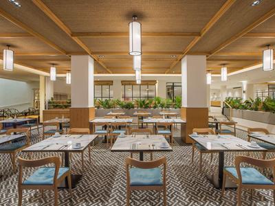 Modernes Restaurant mit Holzbalken, Pflanzen und quadratischen Tischen mit Stühlen.