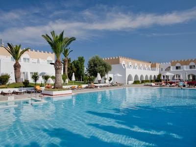 Großer Hotelpool mit Liegestühlen und weißem Gebäude bei sonnigem Wetter.