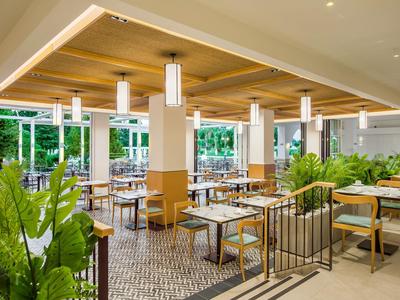 Helles Restaurant mit hölzernen Deckenverkleidungen, weißen Tischen und grünen Pflanzen.