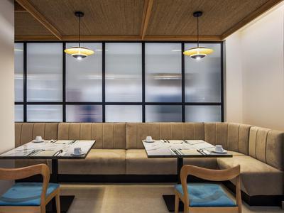 Moderner Essbereich mit Ecksofa in Beige, Holztisch, zwei blauen Stühlen und großen Fensterfronten.