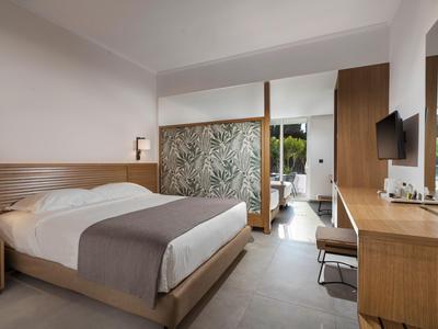 Moderner Hotelzimmer mit großem Bett, Schreibtisch, TV und hellem, minimalistischem Design.
