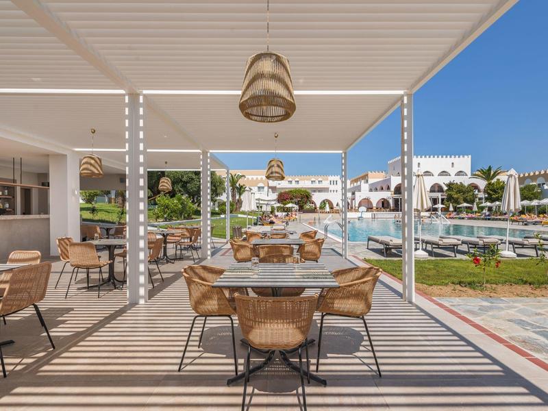 Moderner Außenbereich mit Tischen, Stühlen, Weingläsern, Pool und weißer Architektur im Hintergrund.