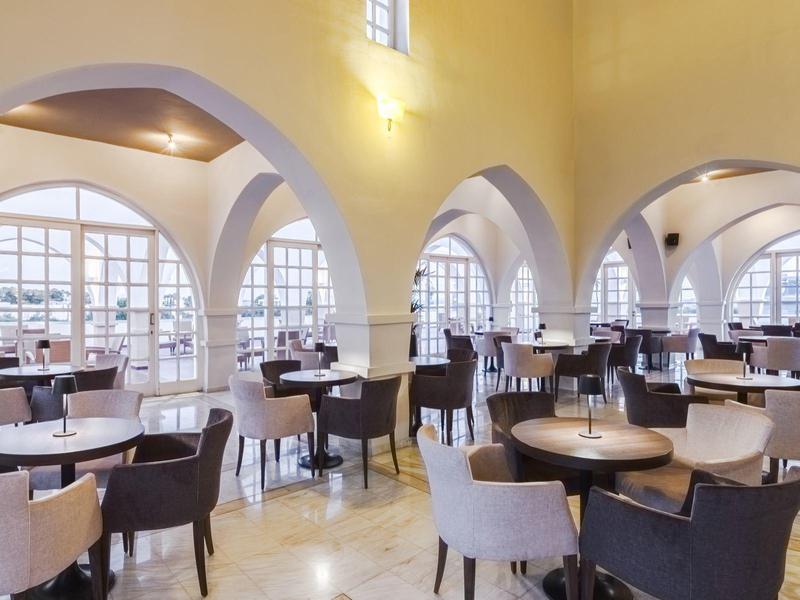 Großer heller Speisesaal mit runden Tischen, gemischten Stühlen und hohen gewölbten Decken.