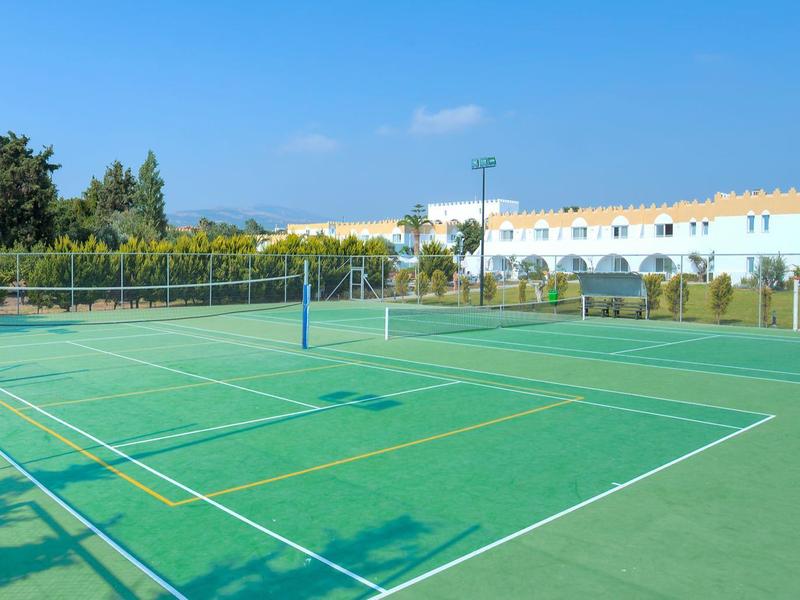 Grüner Tennisplatz im Freien mit blauem Himmel und Gebäuden im Hintergrund.