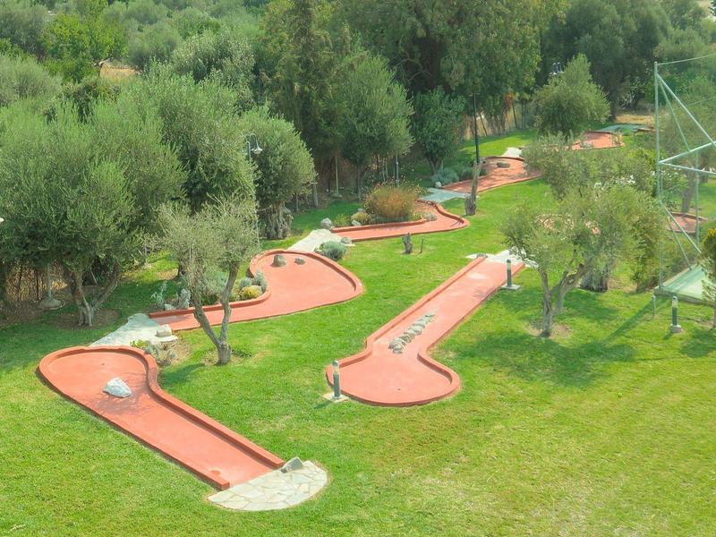 Minigolfanlage mit roten Bahnen, umgeben von grünem Rasen und Bäumen.