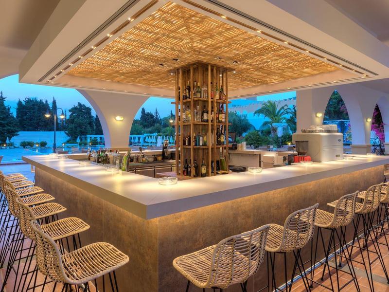 Moderner Außenbarbereich mit Hockerreihen, rustikalem Holz und Abendbeleuchtung am Pool.