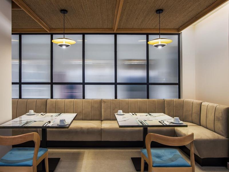 Moderner Essbereich mit Ecksofa in Beige, Holztisch, zwei blauen Stühlen und großen Fensterfronten.