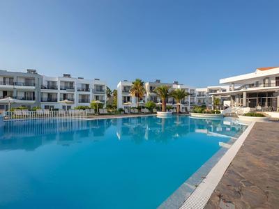 Großer Außenpool vor modernem Hotelgebäude mit klarem blauem Himmel.