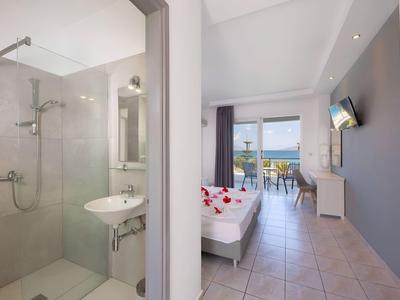 Modernes Hotelzimmer mit Doppelbett, Balkon mit Meerblick und angrenzendem Badezimmer mit Dusche.