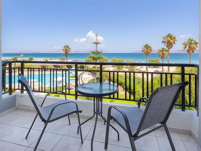 Balkon mit Tisch und Stühlen mit Blick auf Palmen und das Meer unter klarem Himmel.