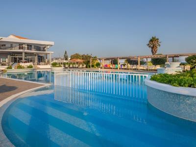 Großer Außenpool mit Terrasse und Hotelgebäude im Hintergrund bei klarem Himmel.
