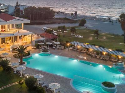 Hotel mit beleuchtetem Pool am Strand bei Sonnenuntergang mit Blick auf das Meer.
