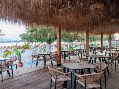 Offene Strandbar mit Strohdach, Holzboden und Tischen mit Stühlen am Meer.