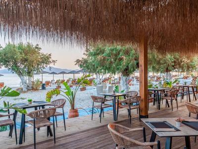 Außerhalb eines Strandrestaurants mit Strohdeckendach und Blick auf Palmen und Meer.