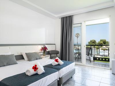 Helles Hotelzimmer mit zwei Einzelbetten und Balkon mit Blick auf das Meer.