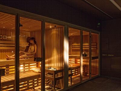 Pohodlná sauna s dřevěnými lavicemi a teplým osvětlením, lidé relaxují uvnitř.