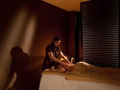 Osoba dostává relaxační masáž v jemně osvětleném spa pokoji s teplými hnědými tóny.