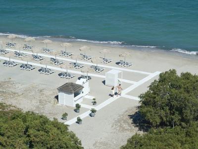 Pláž s řadami lehátek a malým bílým pavilonem u pobřeží.