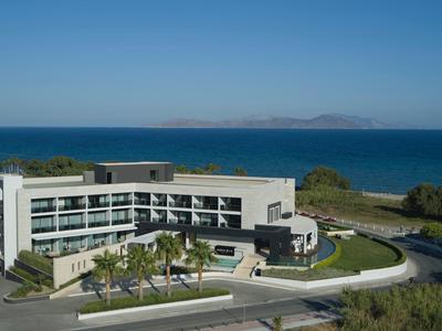 Moderní hotel s obloukovým tvarem u pláže a oceánu pod jasnou modrou oblohou.