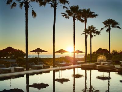 Piscina con lettini e palme al tramonto in un resort tropicale.