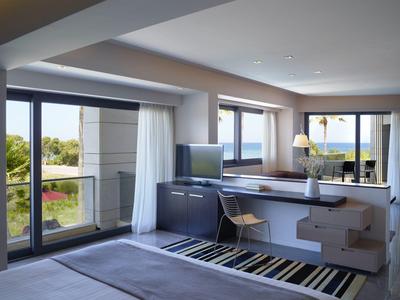 Moderní hotelový pokoj s velkými okny, balkonem, psacím stolem a výhledem na zahradu.