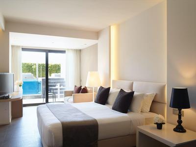 Moderní hotelový pokoj s manželskou postelí, pohovkou a terasou s výhledem na bazén.