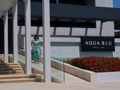 Moderní vstup do hotelu se značkou Aqua Blu, květinami a ženou scházející po schodech