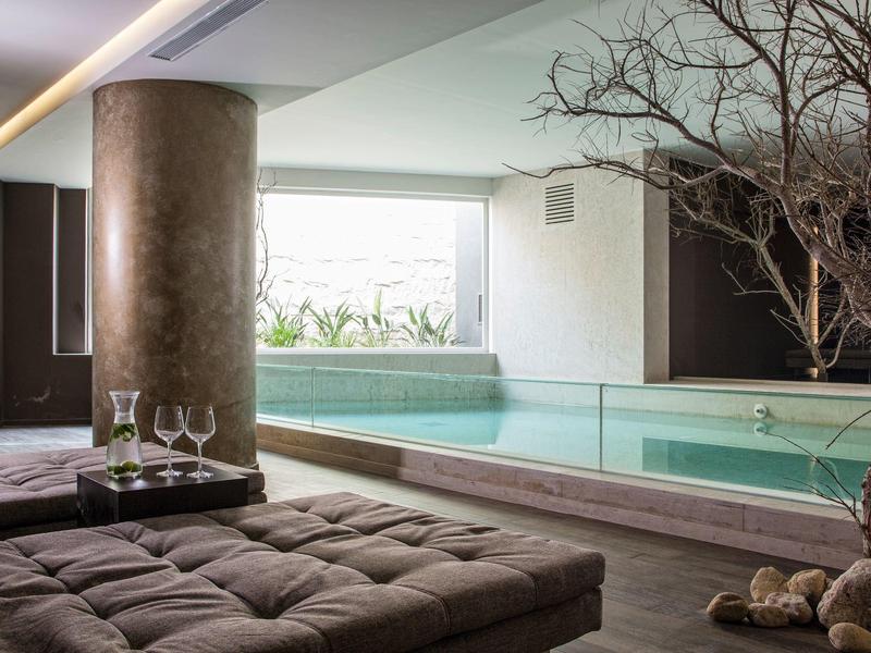 Pohodlný vnitřní prostor s bazénem, prošívanou lavicí, sklem a bezlistým stromem.