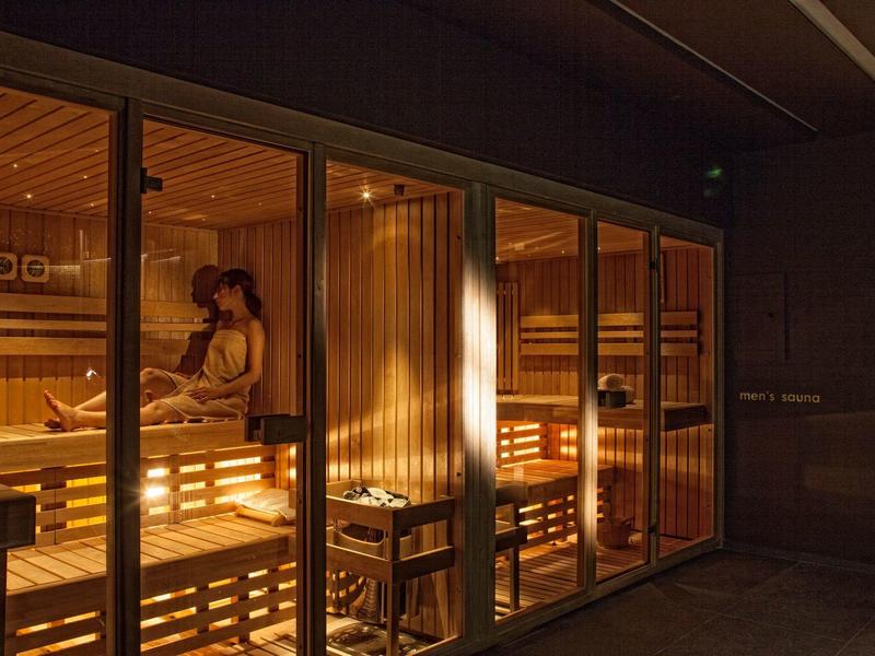 Pohodlná sauna s dřevěnými lavicemi a teplým osvětlením, lidé relaxují uvnitř.