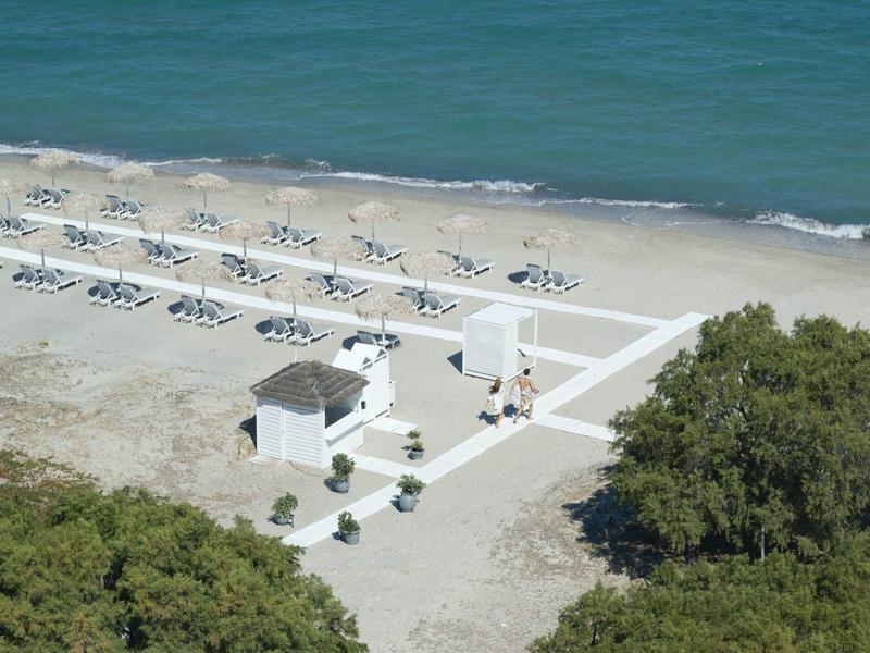 Pláž s řadami lehátek a malým bílým pavilonem u pobřeží.