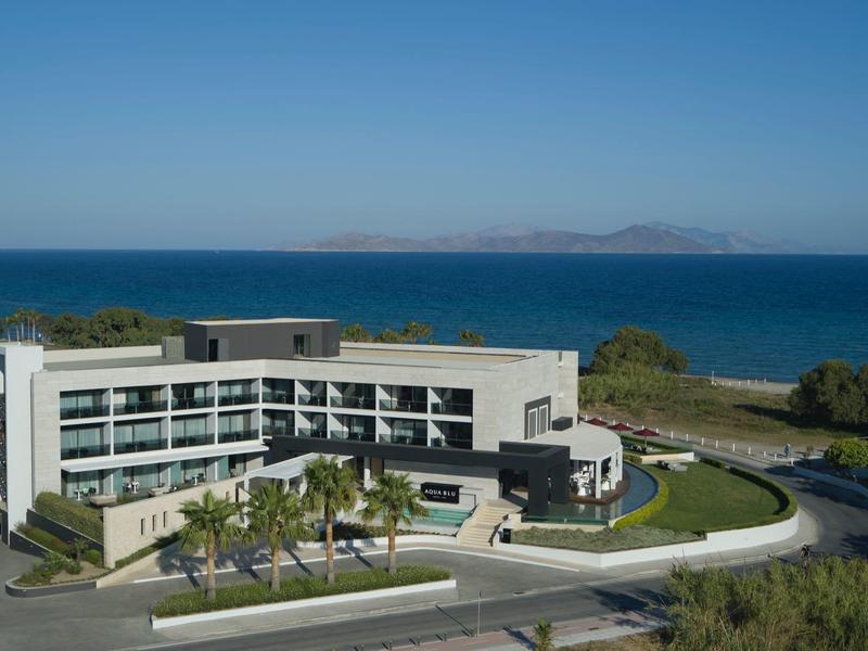 Moderní hotel s obloukovým tvarem u pláže a oceánu pod jasnou modrou oblohou.