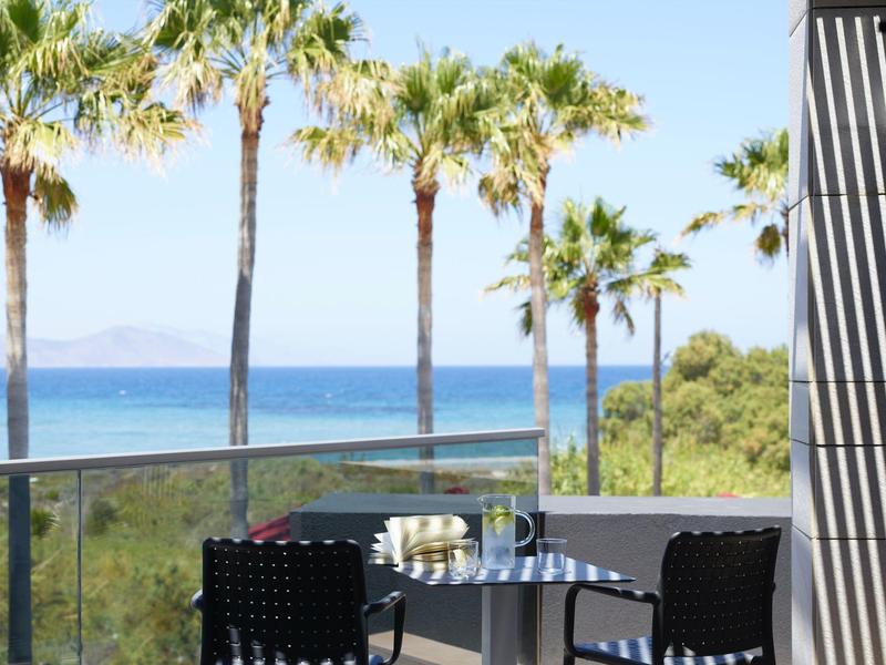 Stůl pro dva s židlemi na balkóně s výhledem na palmy a oceán.