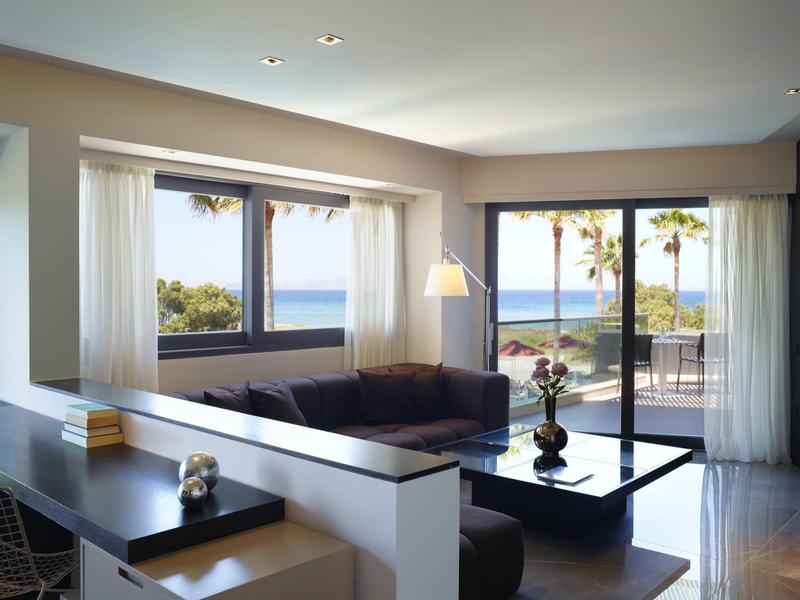 Moderní obývací pokoj s velkými okny s výhledem na moře a palmy, světlý a pohodlný.