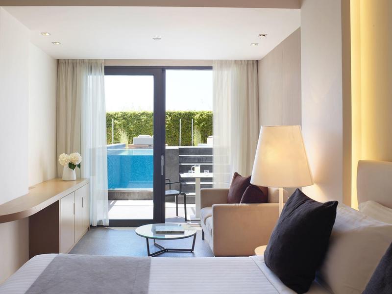 Moderní hotelový pokoj s velkým oknem s výhledem na bazén a terasu.
