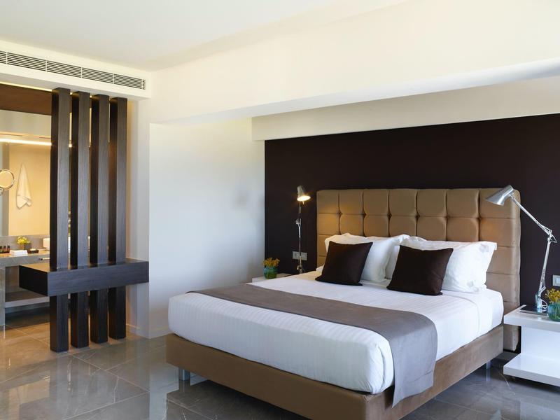 Moderní hotelový pokoj s velkou postelí, nočními stolky a tmavou akcentní stěnou.