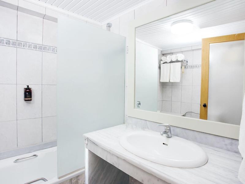 Baño luminoso y limpio con gran espejo y ducha en una habitación de hotel.