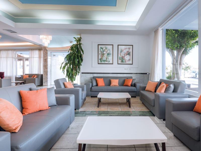Luminosa y moderna sala de hotel con sofás grises y cojines naranjas, grandes ventanas con vista al exterior.