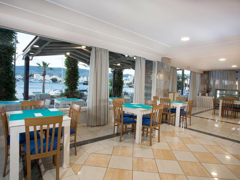 Comedor moderno con mesas y sillas de madera junto a grandes ventanas con vista al mar.