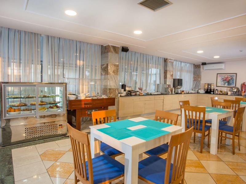 Restaurante de hotel iluminado con sillas de madera, cojines azules y una vitrina con alimentos.