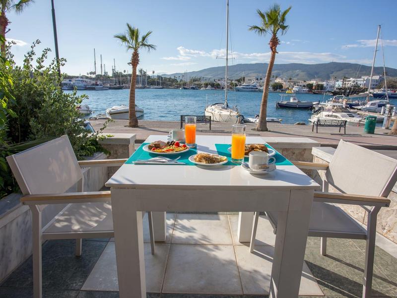 Mesa moderna puesta con vasos naranjas y verdes en el paseo marítimo bajo el sol.