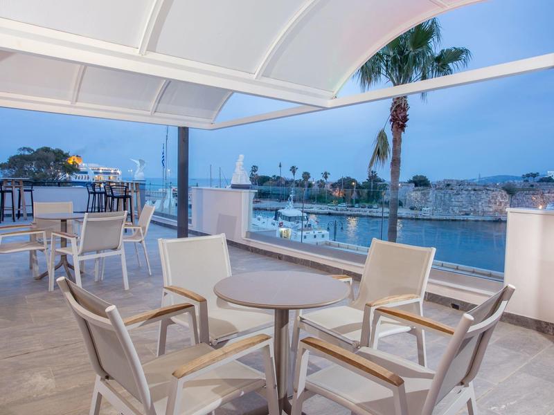 Terraza acogedora con mesas y sillas con vistas a la playa y el mar al atardecer.