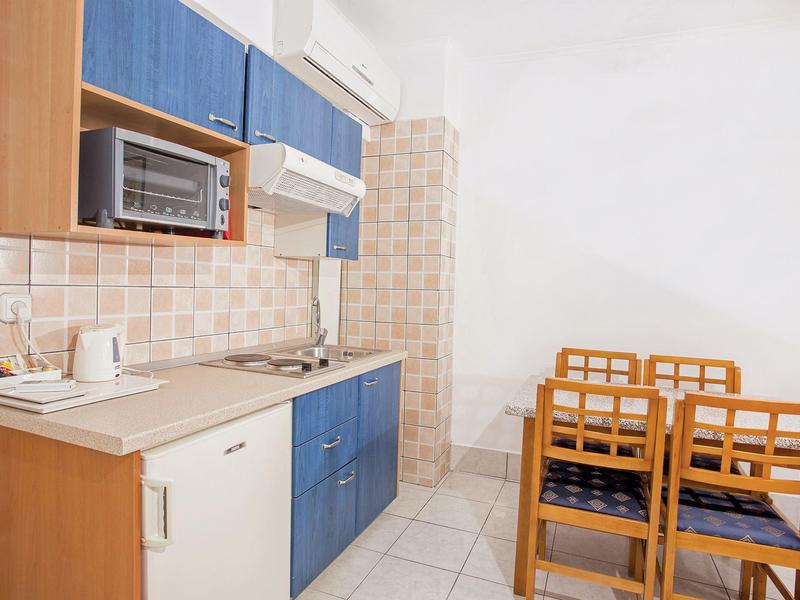 Pequeña cocina con armario azul, microondas y mesa de madera con cuatro sillas en una habitación de hotel.