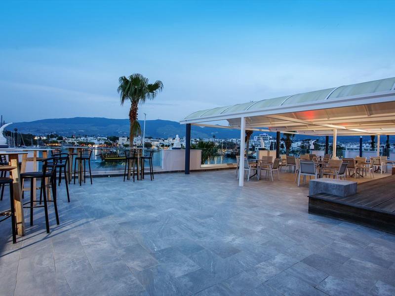 Terraza con taburetes de bar, mesas y vista al mar al anochecer en un hotel.