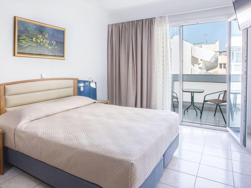 Habitación de hotel luminosa con cama doble, balcón y vista a edificios cercanos.