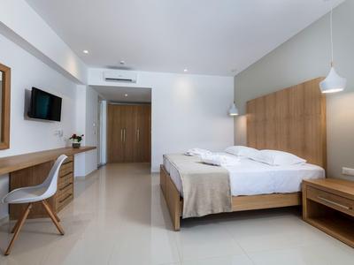 Habitación de hotel luminosa con cama doble, escritorio, silla y televisor en la pared.