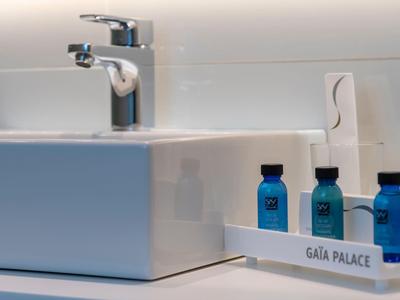 Lavabo blanco con grifo cromado y botellas azules de cosméticos del hotel sobre una bandeja blanca.