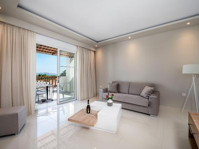 Sala moderna con sofá gris, mesa blanca y acceso a balcón con vista al mar.