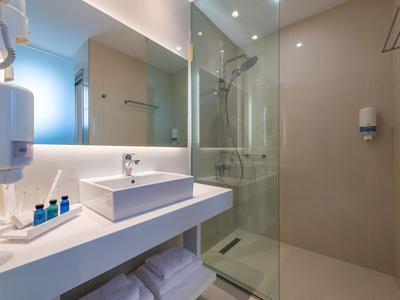 Baño moderno con lavabo, espejo y ducha a la italiana en tonos neutros.